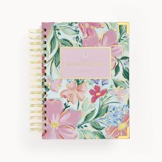 a spiral notebook with pink flowers and green leaves on the cover, sitting against a white background