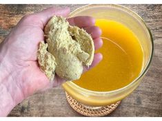 a hand holding a piece of bread next to a bowl of orange liquid on top of a wooden table