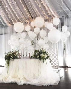 white balloons and greenery are hanging from the ceiling in front of a wedding table