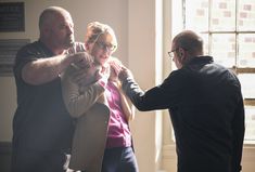 two men and a woman standing next to each other in front of a window with sunlight streaming through them