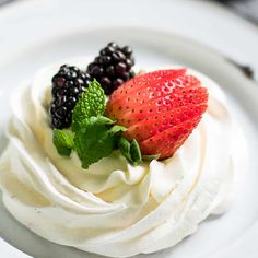 a dessert with whipped cream, berries and mint garnish on a white plate