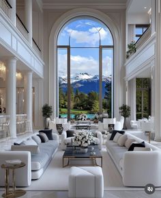 a large living room filled with white furniture and tall windows covered in snow capped mountains