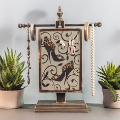 a decorative piece with high heel shoes and pearls hanging from it's sides on a table next to potted plants