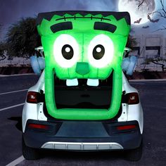 an inflatable green monster is sitting on the back of a white car with it's eyes wide open