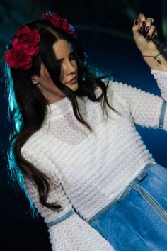 a woman with long hair wearing a white sweater and blue skirt holding a microphone in her hand