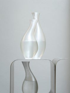 two white vases sitting on top of a metal stand in front of a wall