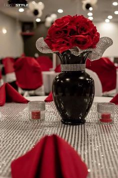 a vase filled with red roses sitting on top of a table covered in silver cloth