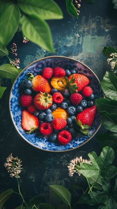 a blue and white bowl filled with berries and strawberries on top of green leaves