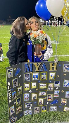 two women kissing each other in front of a sign with balloons and photos on it