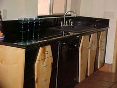 a kitchen with black counter tops and wooden cabinets in the center, along with brown tile flooring