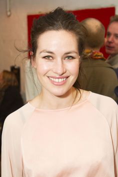 a young woman smiling at the camera while standing in front of other people and wearing a pink top