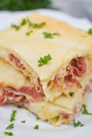 a piece of lasagna with meat and cheese on a white plate, garnished with parsley