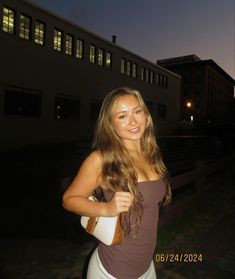 a beautiful young woman standing in front of a building at night with her hand on her hip