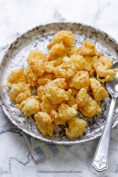 a plate full of tater tots on a marble counter top with a spoon