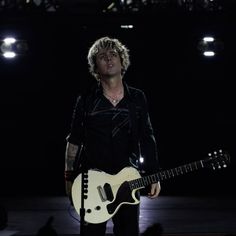 a man standing in front of a microphone and holding a white guitar on top of a stage