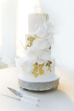 a three tiered white and gold wedding cake with flowers on the top, sitting on a table next to a knife