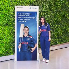 two women standing in front of a green wall with an advertisement for the india cricket team