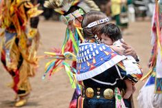 a woman holding a child in her arms while standing next to other people wearing colorful costumes