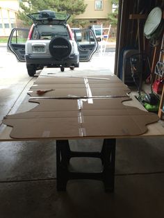 an open garage door with cardboard on the floor and cars parked in the back ground