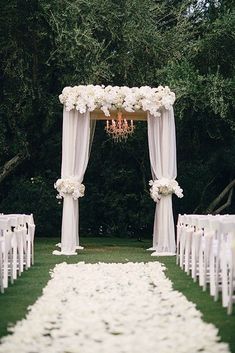 an outdoor wedding ceremony with white flowers on the aisle and chandelier draped over it