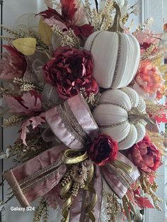 a wreath with flowers and pumpkins hanging on the front door