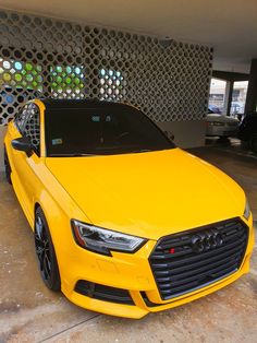 a bright yellow car parked in front of a metal wall with circular holes on it