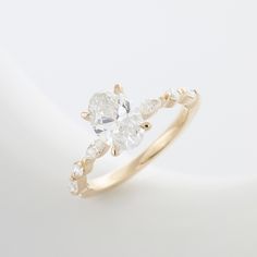 a yellow gold engagement ring with an oval cut diamond and two pear shaped diamonds on the side