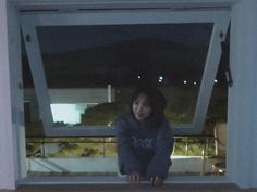 a woman sitting on the floor in front of an open window at night with her feet propped up