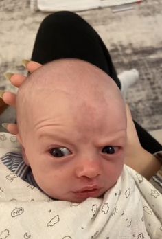 a balding baby is being held up to the side by someone's hand