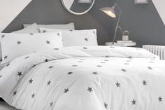 a white bed with black stars on it in a room next to a lamp and mirror