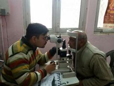 an old man looking through a microscope at another older man sitting in front of him