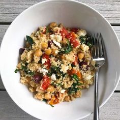 a bowl filled with rice and vegetables on top of a wooden table next to a fork