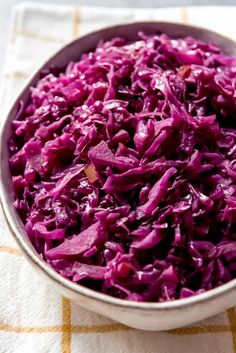 a bowl filled with red cabbage sitting on top of a white table cloth next to a knife