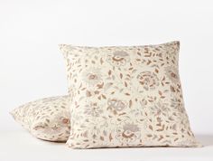 two pillows sitting next to each other on top of a white surface with brown and tan flowers