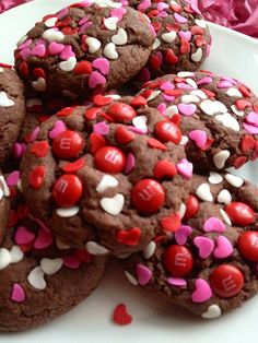 chocolate cookies with red and white sprinkles are on a plate next to pink flowers