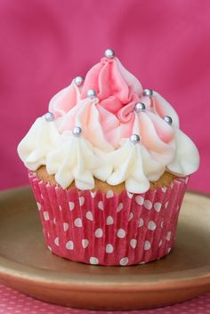 a cupcake with white and pink frosting on a gold plate against a pink background