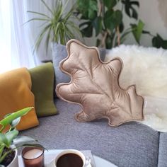 a coffee cup sitting on top of a white plate next to a leaf shaped pillow