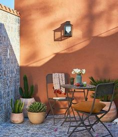 two chairs and a table with potted plants on the side of a building next to a wall