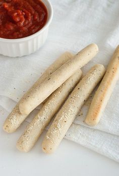 some bread sticks are on a white towel next to a small bowl of tomato sauce