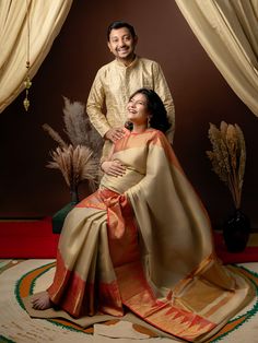 a man standing next to a woman sitting on top of a rug in front of curtains