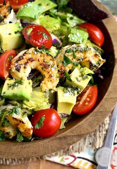 a salad with shrimp, avocado, tomatoes and lettuce in a wooden bowl