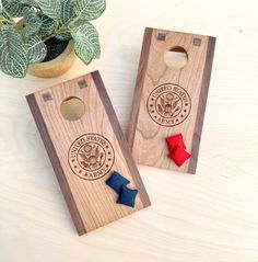 two wooden cornhole game pieces with red, white and blue bows on them next to a potted plant