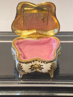 an ornately decorated box with pink velvet lining and gold trimmings sits on a black surface