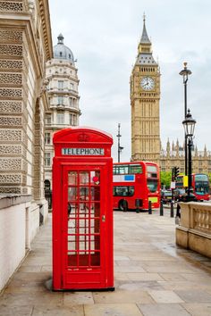 a red phone booth sitting on the side of a street next to a clock tower