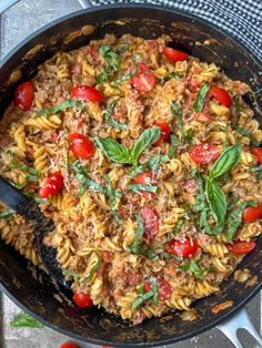 a skillet filled with pasta and tomatoes on top of a table next to utensils