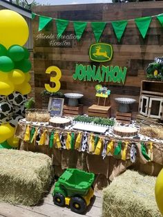 a table topped with hay bales covered in green and yellow balloons next to a wooden wall