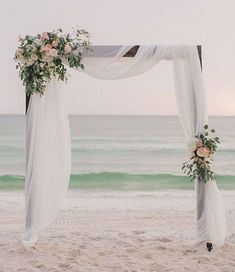 an outdoor wedding setup on the beach with white draping and pink flowers at the top