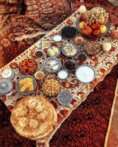 an assortment of food is displayed on a table in front of a persian rug, with bowls of fruit and nuts