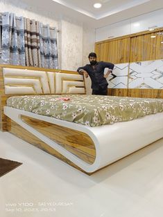 a man standing next to a bed in a room with white walls and wooden furniture