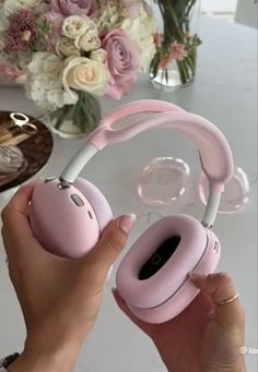 a person holding up pink headphones in front of a vase with flowers on it